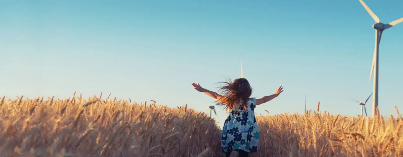a little girl running in a wheat field with arms open with distant Wind turbines in sight